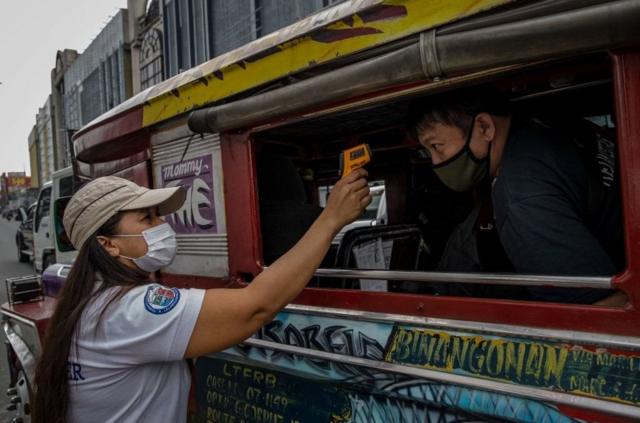 菲律賓擴大封城，政府員工在檢查站檢測吉普車乘客的體溫。