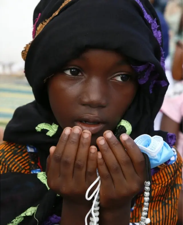 A girl holds prayer beads in her hands as she prays...