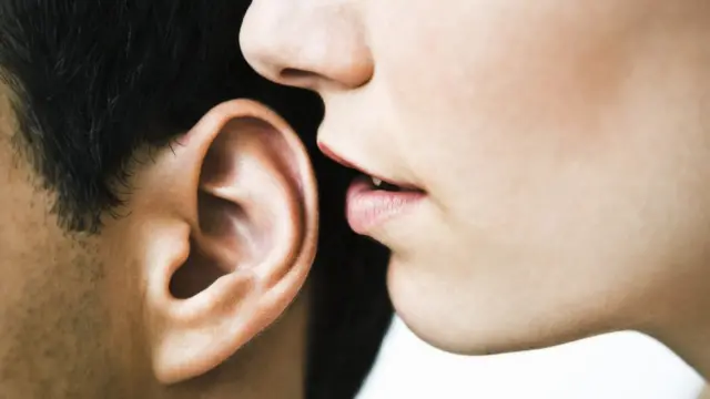 A woman whispers into a man's ear
