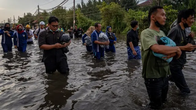 Sejumlah warga yang didominasi pekerja industri kawasan pelabuhan berjalan menembus banjir limpasan air laut ke daratan atau rob yang merendam kawasan Pelabuhan Tanjung Emas Semarang, Jawa Tengah, Senin (23/5/2022).