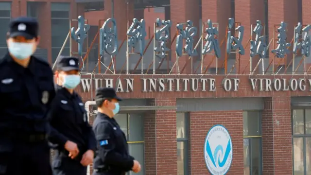 Três agentes fardados esite de aposta que ganha bonusmáscarasite de aposta que ganha bonusfrente a fachada com dizeres: Wuhan Institute of Virology