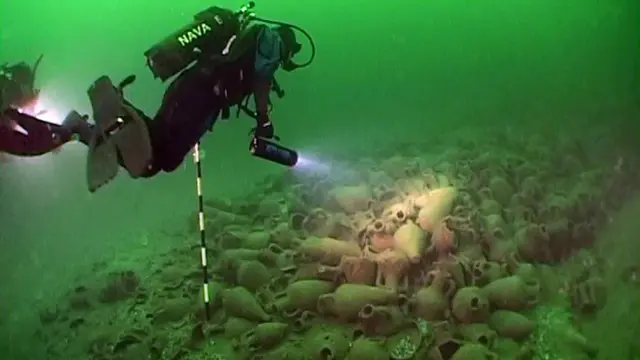 Водолаз з ліхтарем під водою біля сотень старовинних амфор