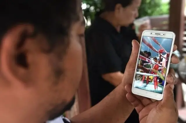 สมศักดิ์ ดีรุจิเจริญ ผู้ฝึกสอนมวยไทย ชมคลิปวิดีโอการชกครั้งสุดท้ายของน้องอนุชา ทาสะโก นักมวยเด็กวัย 13 ปี ระหว่างร่วมงานศพของน้องอนุชาที่วัดใน จ.สมุทรปราการ