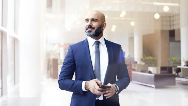 Hombre observa hacia el horizonte con el celular en la mano.