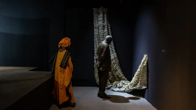 Des spectateurs admirent une œuvre de l'artiste sénégalaise Aissa Dione lors de l'inauguration de la galerie Black Rock. L'œuvre d'art ressemble à une structure en forme de hamac.