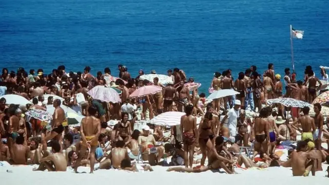 Pessoas tomam sol na praia lotada