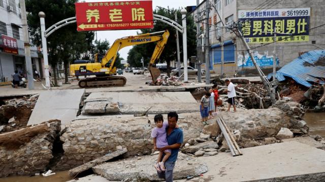 A man holding a child walks across a damaged bridge after the rains and floods brought by remnants of Typhoon Doksuri, in Zhuozhou, Hebei province, China August 7, 2023.