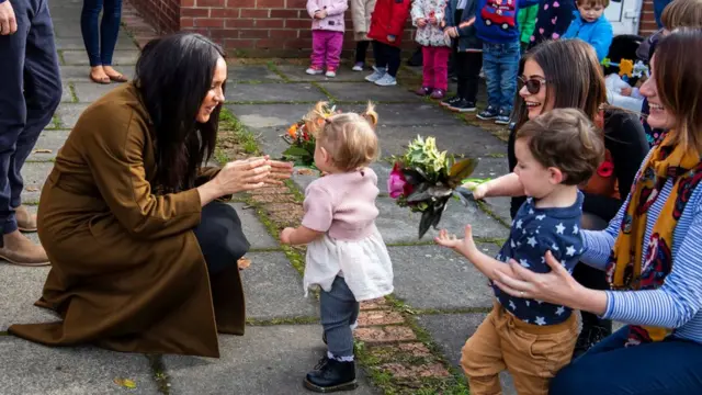 The Duchess of Sussex crouches down to greet a toddler outside Windsor's Broom Farm Community Centre
