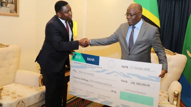 Rais Magufuli akipokea mfano wa hundi yenye thamani ya Sh125m kutoka kwa balozi wa Kenya Dkt. Dan Kazungu