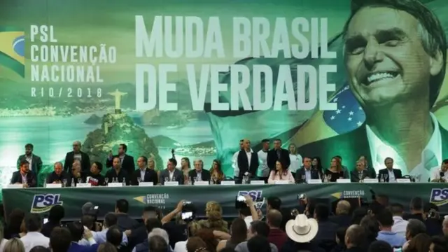 Convenção do PSL tem representantes do partido sentados à mesa sobre palco; no fundo, painel grande com imagemroleta 365 como funcionaBolsonaro e dizeres: 'Muda Brasilroleta 365 como funcionaverdade'