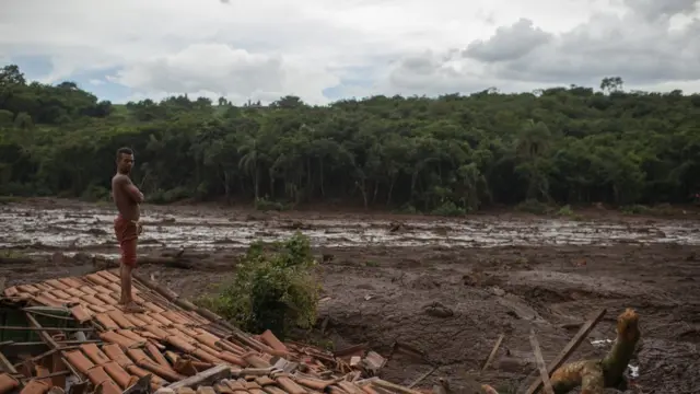 Morador sobre o telhadojogo loteria pelo aplicativosua casa, com o entorno coberto por lama