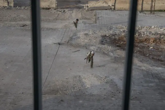 نوجوان مبارز کوبانی در حال ورود به ساختمان مدرسه، خود را از تیررس تک تیراندازهای داعشی دور نگه می دارند.