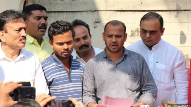 धर्मा पाटील यांचे पुत्र नरेंद्र पाटील लेखी आश्वासन वाचताना, सोबत महाराष्ट्राचे जलसंपदा मंत्री गिरीष महाजन (डावीकडून पहिले) आणि पर्यटनमंत्री जयकुमार रावल (उजवीकडे)