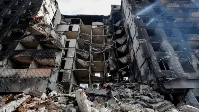 An emergency worker strides across rubble in front a a destroyed building