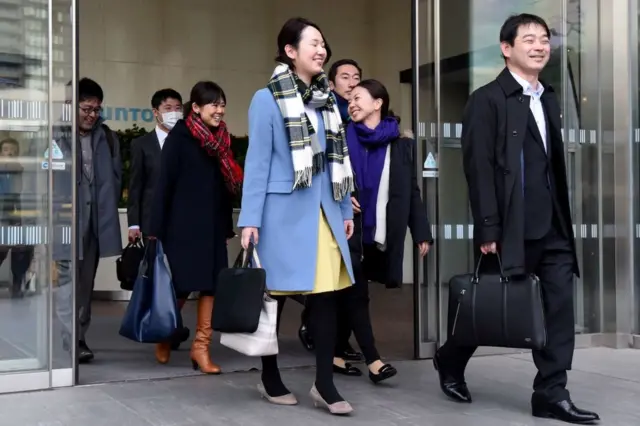 Trabajadores japoneses salen de la empresa sonriendo.