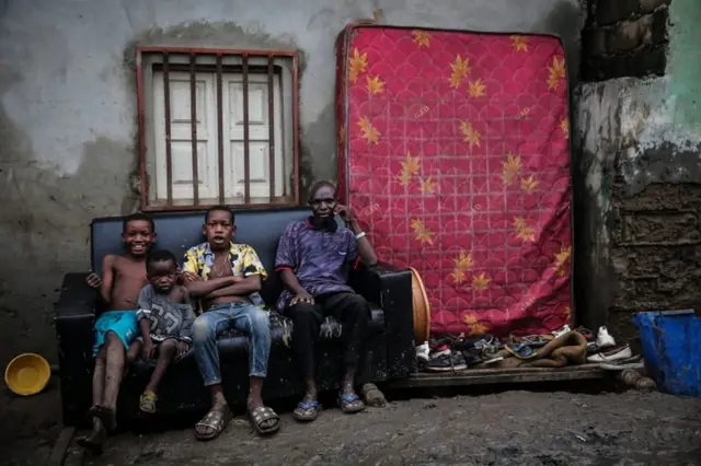 People sit on a sofa outside their house with their belongings.