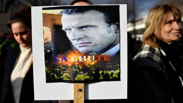 A woman holds a placard bearing a photo of French President Emmanuel Macron with the words "La Chute" (The Fall) during a protest against the pension overhauls, in Marseille, southern France, on 5 December, 2019.