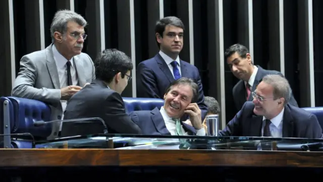 Senadores conversam e sorriem na mesa do plenário do Senado