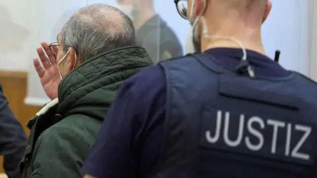 ضابط المخابرات السورية السابق أنور رسلان (إلى اليسار) يقوده ضابط قضائي إلى قاعة محكمة في كوبلنز، غرب ألمانيا، في 13 يناير/كانون الثاني 2022