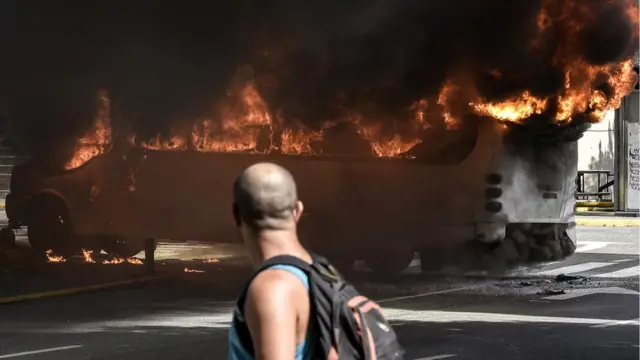 Hombre mira a un bus en llamas.