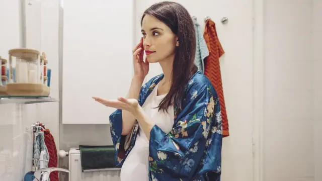 Mujer embarazada se mira la piel en un espejo