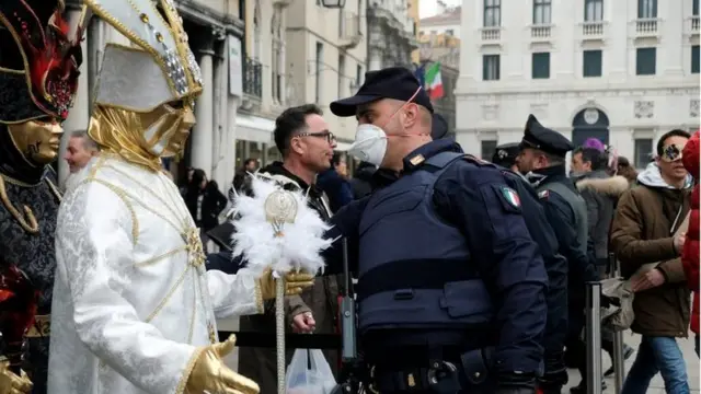 Police officer wearing a protective face mask stands next to carnival revellers at Venice Carnival