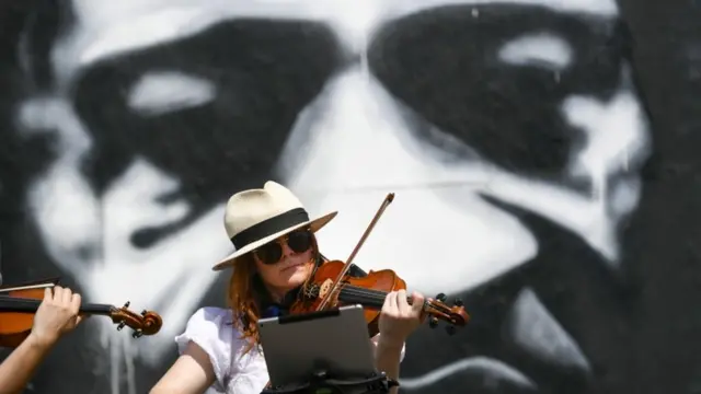 Mulher toca violino em frente a grande foto do rosto de Floyd