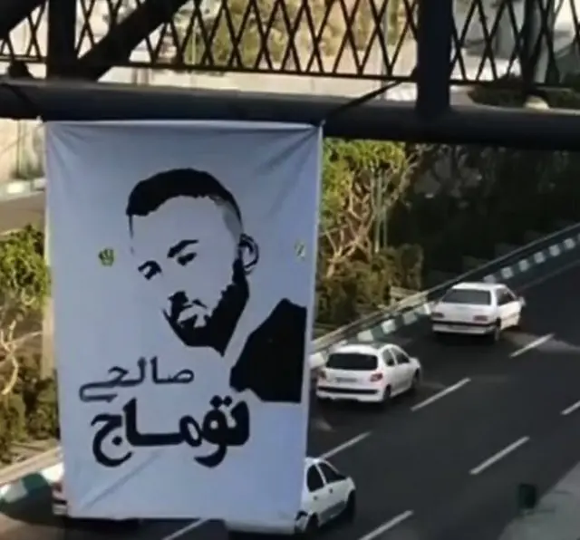 A placard with Toomaj Salehi's photo over a motorway bridge