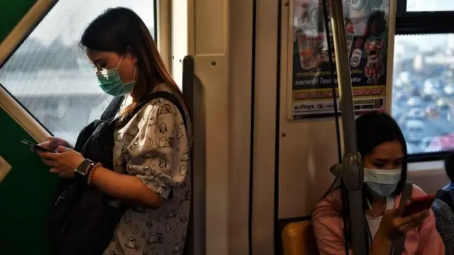Commuters, wearing facemasks amid concerns over the spread of the COVID-19 novel coronavirus, take the BTS Skytrain in Bangkok on March 4, 2020