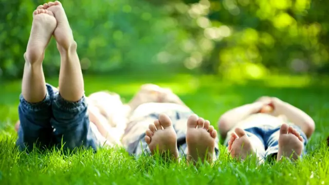 Tres personas de pies descalzos tumbadas en la hierba.