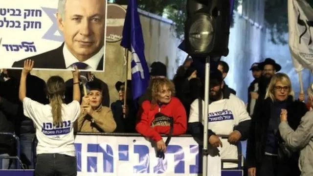 Supporters of Mr Netanyahu stand outside the prime minister's residence with signs