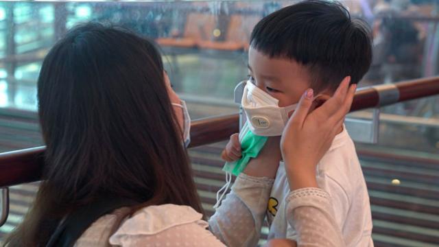 Uma mulher usando uma máscara ajuda seu filho a colocar sua máscara no aeroporto de Changi em 25 de janeiro de 2020 em Cingapura