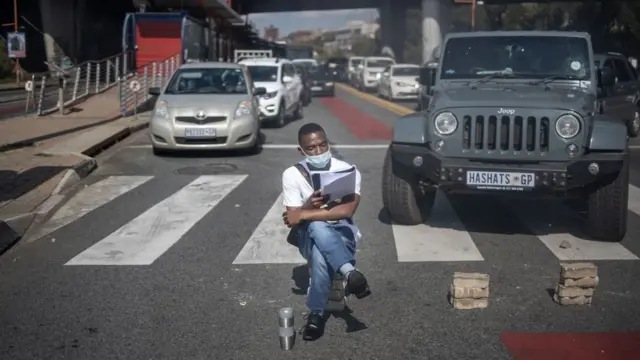 A man sits on bricks pretending to read as students members of the African National Congress (ANC) and the Economic Freedom Fighters (EFF) block traffic in Braamfontein, Johannesburg, South Africa - Wednesday 10 March 2021