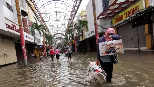 Warga melintasi banjir menggenangi pertokoan Pasar Baru, Jakarta Pusat, Selasa (25/02)