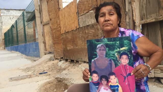 Irma Vargas Laguna en la puerta de su casa en Ciudad Juárez con una foto de su hija y sus nietos
