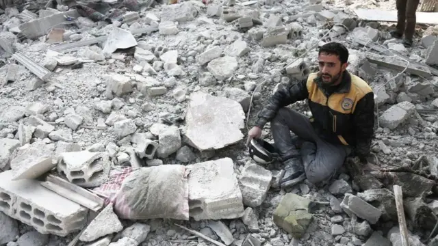 બોમ્બમારામાં ધરાશાયી થયેલી ઇમારતના કાટમાળની વચ્ચે બેઠેલો વ્યક્તિ