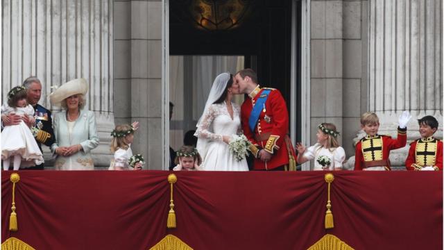 Prince William and Kate Middleton kiss on the balcony of Buckingham Palace on their wedding day, surrounded by their wedding party.