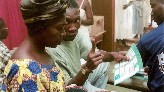 Un volontaire explique à une femme qu'elle peut valider son bulletin en signant ou posant ses empreintes lors de l'élection présidentielle de 2000 en Côte d'Ivoire.