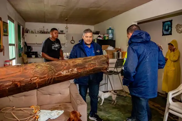 Imagen en la que se observa a funcionarios del Departamento de la Familia visitando a Sonalee y el árbol que penetró la ventana de su residencia.