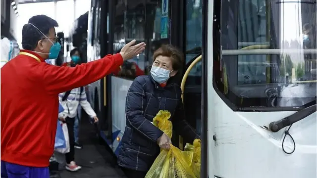 Um oficial usando uma máscara gesticula para uma mulherhandicap estrela betmeia-idade enquanto ela entrahandicap estrela betum ônibus segurando uma grande sacola plástica com pertences