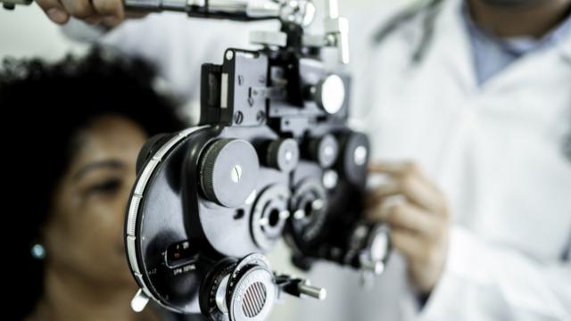Mulher sentada, sendo examinada por médico com equipamento para diagnóstico nos olhos