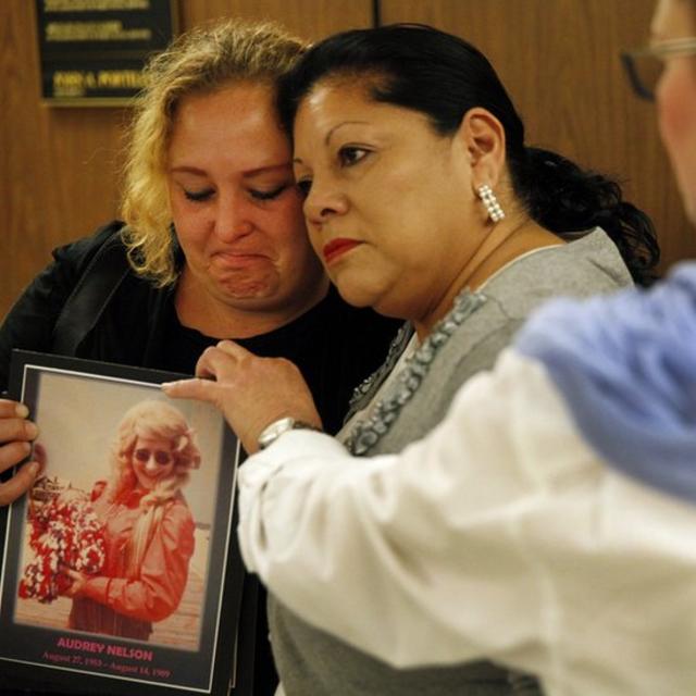 Loved ones of two of his victims embrace at 2014 trial, holding an image.
