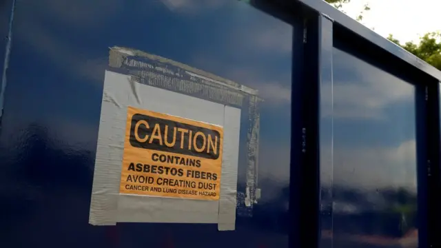 Предупреждающий об опасности знак на мусорном контейнере рядом с местом переработки асбеста. И вы сюда переведете свой бизнес?