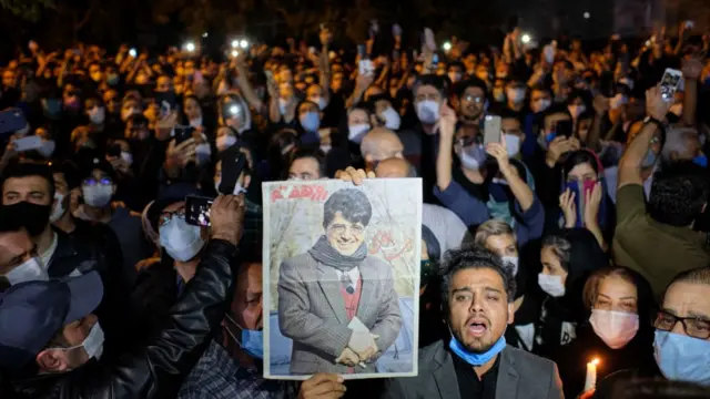 Kalabalığın önünde Şeceryan posteri taşıyan bir adam.