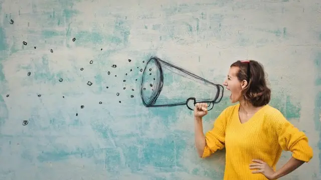 Young woman holding an imaginary megaphone and shouting into it