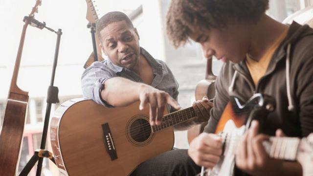 Um homem ensinando um adolescente a tocar violão/guitarra