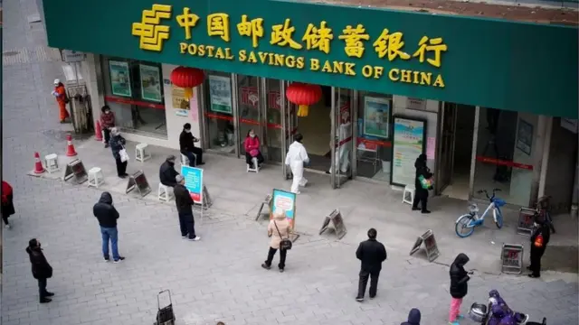 People wearing face masks practise social distancing as they wait outside a Postal Savings Bank of China branch in Wuhan, Hubei province,