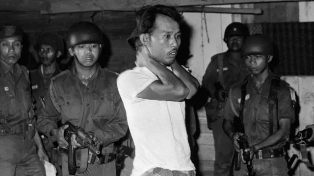 A suspected sympathizer with the Communist-led abortive coup of October 1th is questioned under gunpoint. The Indonesian Army is continuing its careful screening in an effort to uproot dissenters.