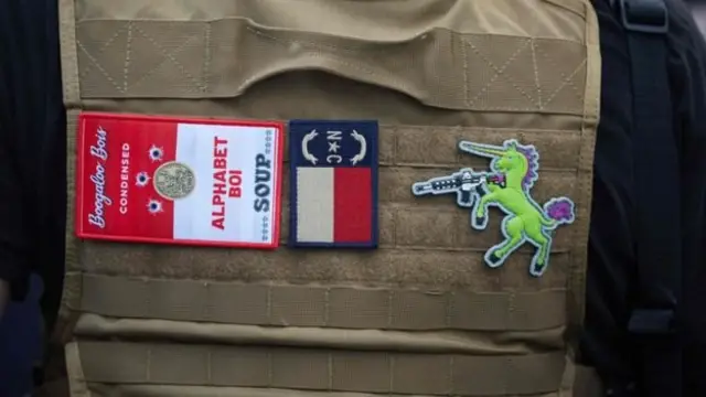 Les membres du Boogaloo Bois portent souvent en public des chemises hawaïennes et des tenues militaires rapiécées par le Boogaloo. "Alphabet" est une référence aux agences fédérales américaines qui utilisent des acronymes, comme le FBI