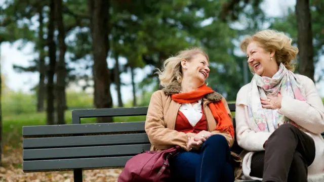 Dos mujeres sonriendo en un banco.